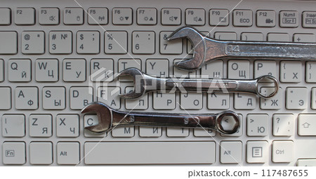 Engineering And Computer Hardware Concept. Three shiny mechanical wrenches laid out in order on computer keyboard top view Engineering And Computer Hardware Concept. Three shiny mechanical wrenches laid out in order on computer keyboard top view 117487655