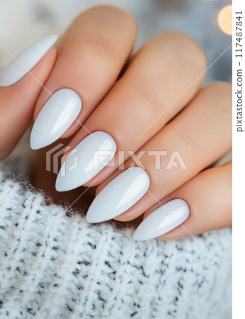 Elegant white manicure displayed on a cozy knitted sweater in a softly lit setting 117487841