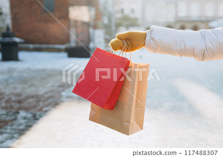 Cropped unrecognizable Woman Holding a red shopping bags, Celebrating Christmas. Female holding a presents ready to celebrate winter holidays at city street. Mock up 117488307