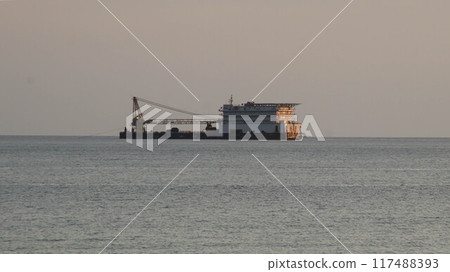 Seen far at the horizon an offshore vessel barge transportation with support crane for building and support offshore oil rig drilling site, in the middle of the ocean, in the evening. 117488393