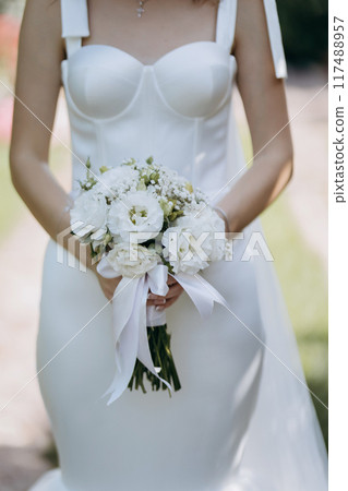 Elegant bride holding a white floral bouquet in a minimalist wedding gown, symbolizing purity 117488957