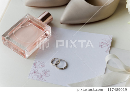 Bride's wedding essentials: heels, bouquet, rings, perfume, and invitation on a white table Bride's wedding essentials: heels, bouquet, rings, perfume, and invitation on a white table 117489019