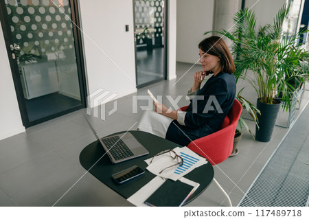 In a contemporary office, a modern businesswoman is utilizing her smartphone for work 117489718