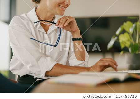 A dedicated Professional Woman Working at Her Desk with Glasses, Focused on Success and Growth A dedicated Professional Woman Working at Her Desk with Glasses, Focused on Success and Growth 117489729
