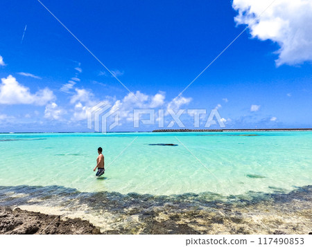 A man in a swimsuit walking with the beautiful ocean of Kumejima in the background A man in a swimsuit walking with the beautiful ocean of Kumejima in the background 117490853