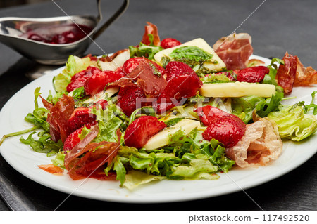 Salad with fresh strawberries, prosciutto, and mixed greens, topped with a light vinaigrette 117492520