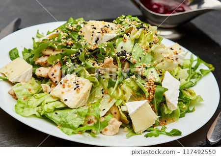 Fresh green salad with chicken, brie cheese, and sesame seeds, served with berry sauce on the side Fresh green salad with chicken, brie cheese, and sesame seeds, served with berry sauce on the side 117492550