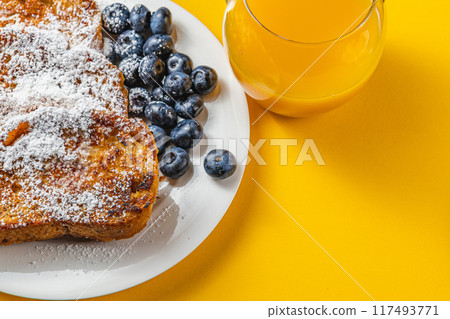 French toast on a white plate with blueberries and orange juice for breakfast 117493771