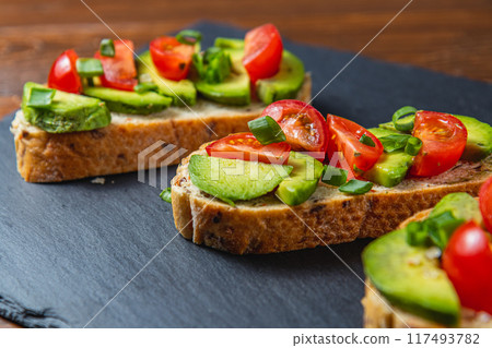 Avocado toast topped with tomato and green onion on a slice of carrot bread 117493782