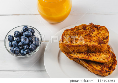 French toast on a white plate with blueberries and orange juice for breakfast French toast on a white plate with blueberries and orange juice for breakfast 117493863