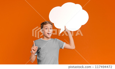 Inspired boy having idea, pointing finger up and holding blank speech bubble, orange studio background 117494472