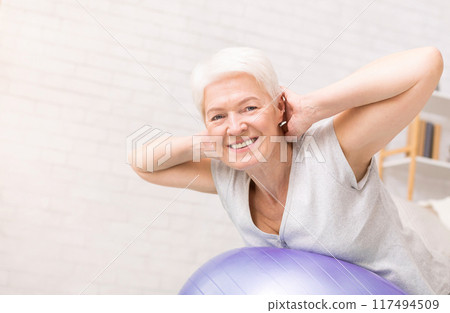 Happy active mature woman doing exercises with fitness ball at home, free space Happy active mature woman doing exercises with fitness ball at home, free space 117494509