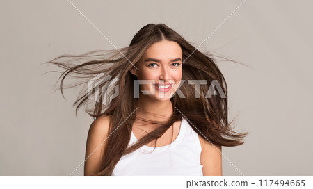 A young woman stands with her hair flowing in the wind. The wind gently tousles her hair as she looks off into the distance. Her hair is lifted and carried by the air A young woman stands with her hair flowing in the wind. The wind gently tousles her hair as she looks off into the distance. Her hair is lifted and carried by the air 117494665