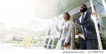 Happy confident african american business people walking out of modern office center after successful meeting. Low-Angle Shot with copy space Happy confident african american business people walking out of modern office center after successful meeting. Low-Angle Shot with copy space 117494743