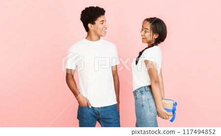 I have surprise. Girl hiding present from boyfriend over pink background 117494852