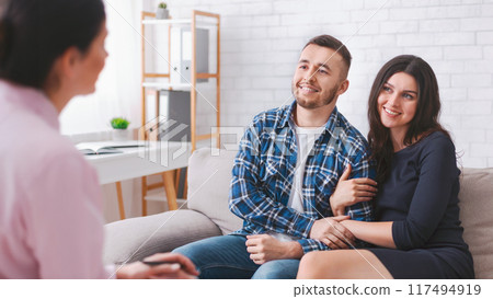 A young couple sits on a couch in a therapists office, listening intently to their counselor, who is out of focus in the foreground. A young couple sits on a couch in a therapists office, listening intently to their counselor, who is out of focus in the foreground. 117494919