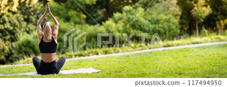 Back view of athletic blonde woman practicing yoga at public park, unrecognizable well-fit lady sitting on fitness mat, holding hands above her head, panorama with copy space Back view of athletic blonde woman practicing yoga at public park, unrecognizable well-fit lady sitting on fitness mat, holding hands above her head, panorama with copy space 117494950