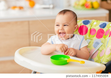 A cute baby boy is sitting in a child chair in the kitchen. The scene is bright and cheerful, focusing on the innocence and happiness of a child at home. A cute baby boy is sitting in a child chair in the kitchen. The scene is bright and cheerful, focusing on the innocence and happiness of a child at home. 117495004
