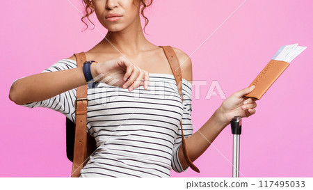 Tourist late for plane, looking at watch and holding tickets over pink background Tourist late for plane, looking at watch and holding tickets over pink background 117495033