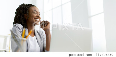 Joyous African American businesswoman at her desk, using a laptop in a stylish office environment, panorama with copy space 117495239