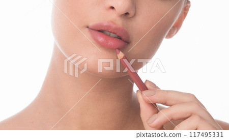 A woman carefully applies a lip liner pencil to define and shape her lips. The close-up shot highlights her precision and focus, cropped 117495331