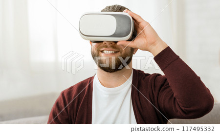 A man with a beard is immersed in virtual reality, wearing a headset that covers his eyes, focused on the virtual experience, with a facial expression reflecting concentration and engagement. 117495332