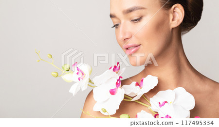 A woman holding a bouquet of white orchids in her hands, showcasing the delicate and elegant flowers on a neutral background, closeup, copy space 117495334