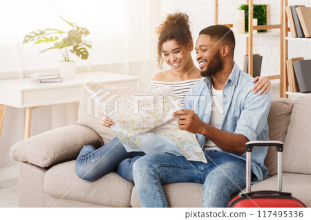 Newlyweds choosing place for honeymoon with map, sitting on sofa 117495336