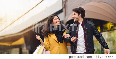 Loving young couple walking with shopping bags at weekend outdoors, talking and enjoying autumn day Loving young couple walking with shopping bags at weekend outdoors, talking and enjoying autumn day 117495367