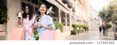 Two Happy Multiethnic Girlfriends Walking With Shopping Bags On City Street, Young Cheerful Women Carrying Purchases And Drinking Takeaway Coffee, Enjoying Seasonal Sales, Copy Space Two Happy Multiethnic Girlfriends Walking With Shopping Bags On City Street, Young Cheerful Women Carrying Purchases And Drinking Takeaway Coffee, Enjoying Seasonal Sales, Copy Space 117495368