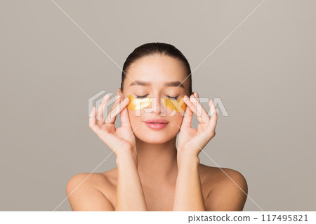 A woman is seen with gold eye masks placed on her face. The masks shimmer in the light, providing a luxurious and rejuvenating skincare experience. The woman appears relaxed and pampered. A woman is seen with gold eye masks placed on her face. The masks shimmer in the light, providing a luxurious and rejuvenating skincare experience. The woman appears relaxed and pampered. 117495821