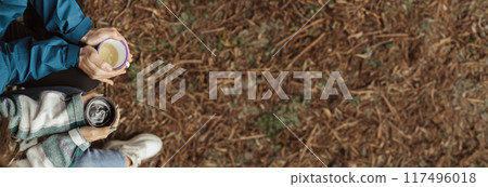 Young caucasian couple in jackets relaxing, drinking cup of coffee, enjoy free time, weekend in cold forest in autumn, close up, top view, cropped. Lifestyle, vacation together outdoor, copy space Young caucasian couple in jackets relaxing, drinking cup of coffee, enjoy free time, weekend in cold forest in autumn, close up, top view, cropped. Lifestyle, vacation together outdoor, copy space 117496018