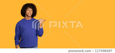 This image shows a man wearing a blue sweatshirt standing against a yellow backdrop. He is smiling and pointing to the right side of the frame with his right hand, copy space This image shows a man wearing a blue sweatshirt standing against a yellow backdrop. He is smiling and pointing to the right side of the frame with his right hand, copy space 117496097