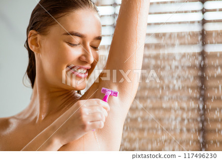 Young woman shaving underarms with razor, taking shower. Unwanted hair detected concept 117496230