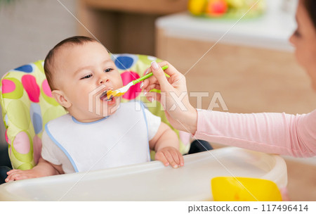 A mother and her baby boy are sharing mealtime in the kitchen, with the baby in a high chair. The atmosphere is nurturing and intimate, reflecting family warmth. 117496414