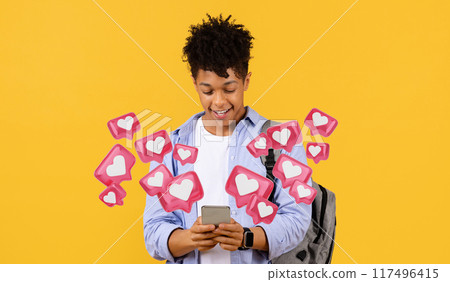 Cheerful black man student engages with smartphone, wearing blue shirt and carrying backpack, against vibrant yellow background. Dating mobile app 117496415