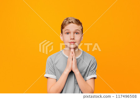 Cute little boy begging for his request, holding hands together, orange studio background 117496508