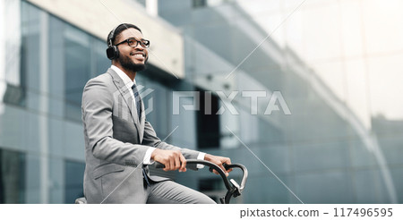 Black businessman is riding his bike to work downtown. The atmosphere is modern and vibrant, reflecting a commitment to both work and sustainable living. 117496595