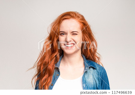 A cheerful young woman with flowing red hair is captured mid-laugh, exhibiting a toothy smile and squinted eyes that express genuine joy A cheerful young woman with flowing red hair is captured mid-laugh, exhibiting a toothy smile and squinted eyes that express genuine joy 117496639