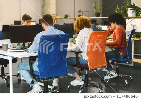 Back view of diverse group of individuals are sitting around a table, each focused on their laptop screens, typing and clicking away Back view of diverse group of individuals are sitting around a table, each focused on their laptop screens, typing and clicking away 117496640