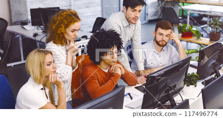 A group of focused multiethnic colleagues are seated at desks using desktop computers in a well-lit, contemporary office. They appear to be engrossed in work, displaying concentration and teamwork A group of focused multiethnic colleagues are seated at desks using desktop computers in a well-lit, contemporary office. They appear to be engrossed in work, displaying concentration and teamwork 117496774