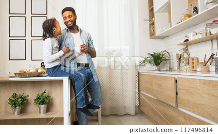 Healthy breakfast together. Happy african dad and daughter having morning meal in kitchen, talking and smiling, copy space, side view 117496814