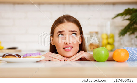 Dieting Concept. Young Woman Choosing Between Fruits and Sweets 117496835