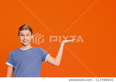 Hesitant boy spreading hands sideways, making choice or decision, cannot choose, orange background with empty space 117496856