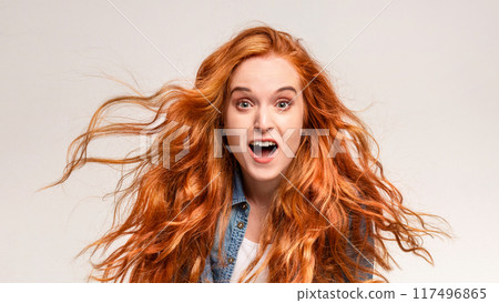 A woman with vibrant red hair is contorting her face into a humorous expression. Her eyes are wide and playful, adding to the comical nature of the moment. 117496865
