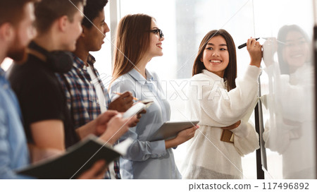 Girl showing answers on whiteboard in classroom with classmates standing around Girl showing answers on whiteboard in classroom with classmates standing around 117496892