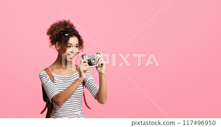 African American woman holding a camera up to her eye, framing a shot with her hands. She is focusing on capturing a moment in time through the lens of the camera, copy space 117496950