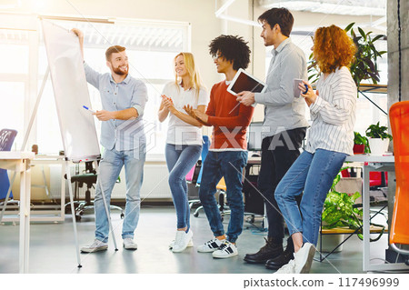 A group of diverse individuals standing in a circle around a white board, engaged in discussion and collaboration. They are pointing, writing, and brainstorming ideas together in a meeting A group of diverse individuals standing in a circle around a white board, engaged in discussion and collaboration. They are pointing, writing, and brainstorming ideas together in a meeting 117496999