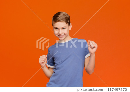 Sly boy making silly grimace, thinking about joke, orange panorama background with empty space 117497270