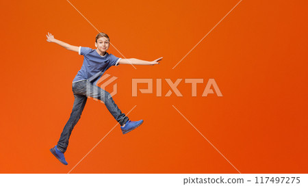 Smiling little boy jumping on orange studio background Smiling little boy jumping on orange studio background 117497275